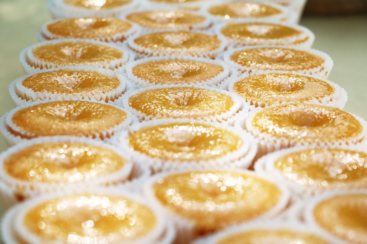 Fila de coininhas douradas e envernizadas em forminhas de papel frisado, sob luz quente.