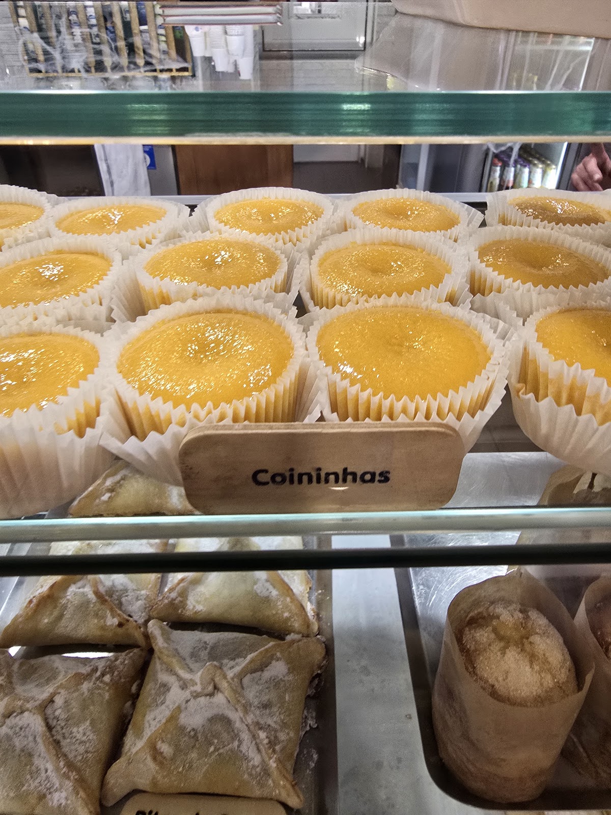 Tabuleiro de coininhas na vitrine refrigerada, com a plaquinha de madeira escrita 'Coininhas'.