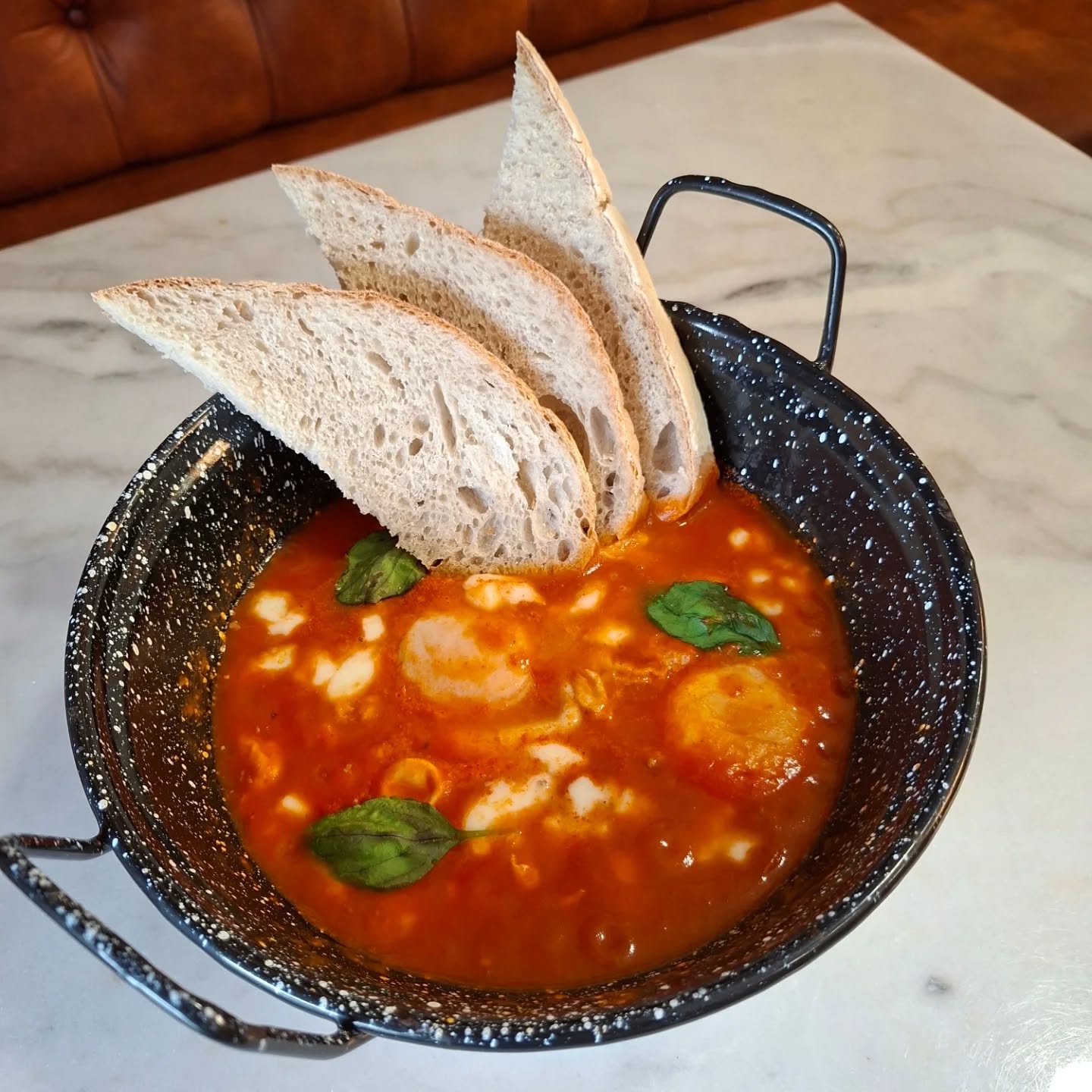 Pão rústico artesanal servido com um prato de ovos em molho de tomate e manjericão.