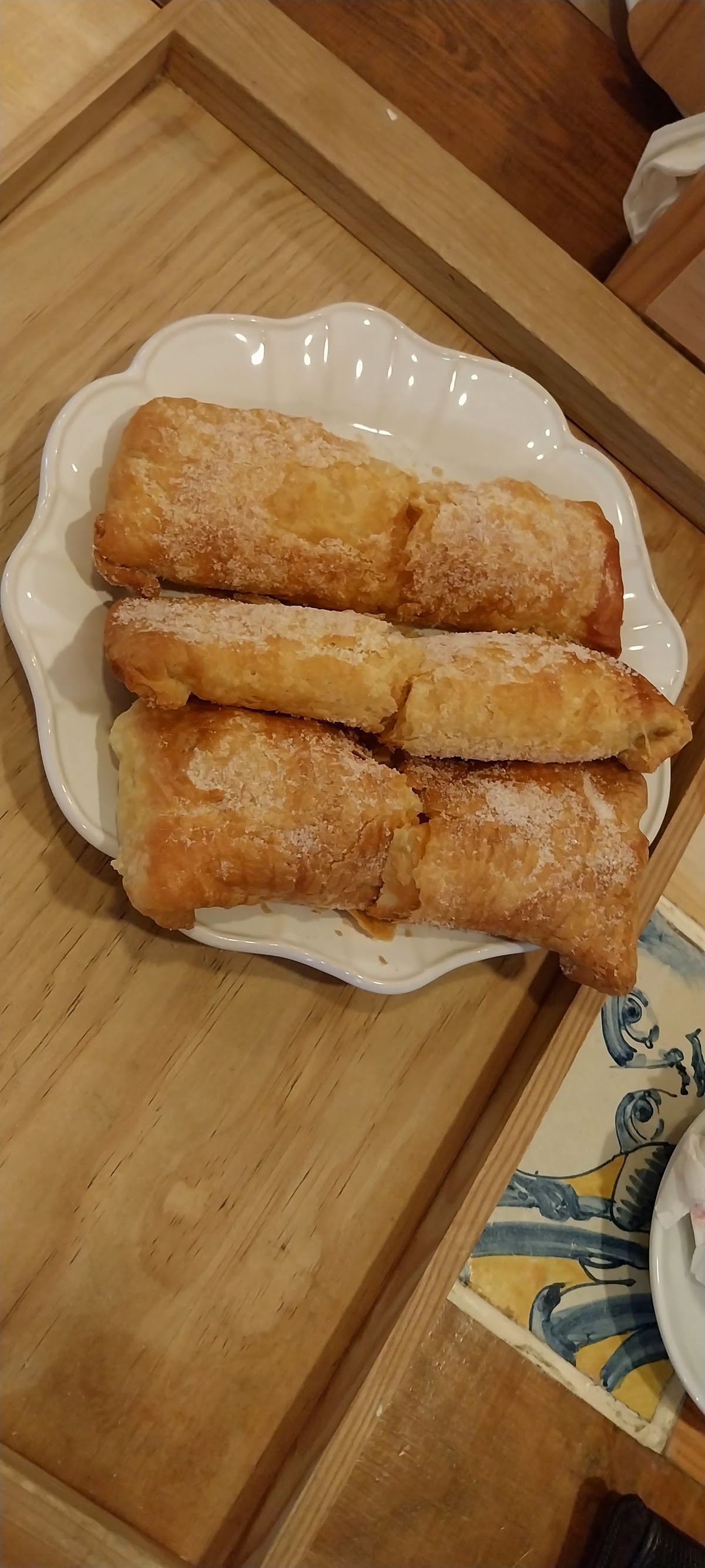 Travesseiros de Coina polvilhados com açúcar, num prato rendilhado sobre tábua de madeira.